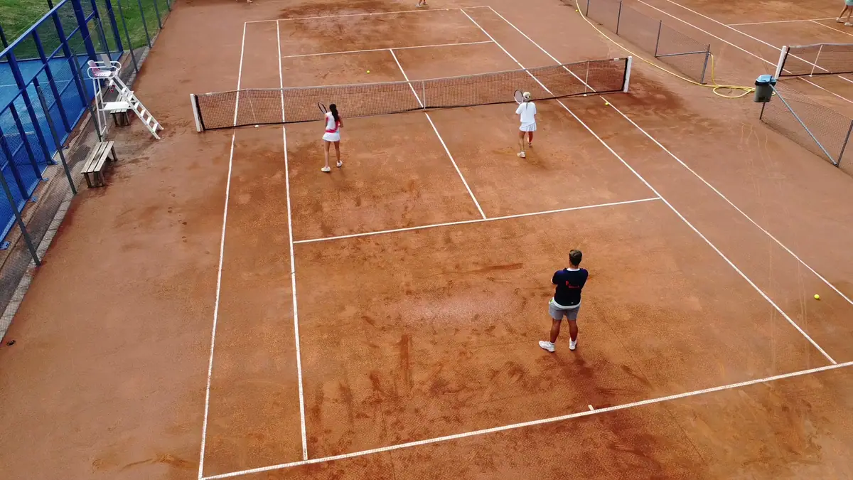 Grusbanan snett ovanifrån med tre spelare i träning och padelbanan i kanten