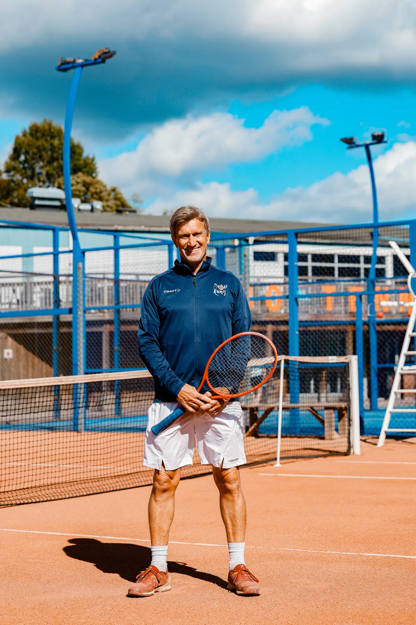 Johan Alvén med orange racket på grusbanan framför padelbanan och klubbhuset