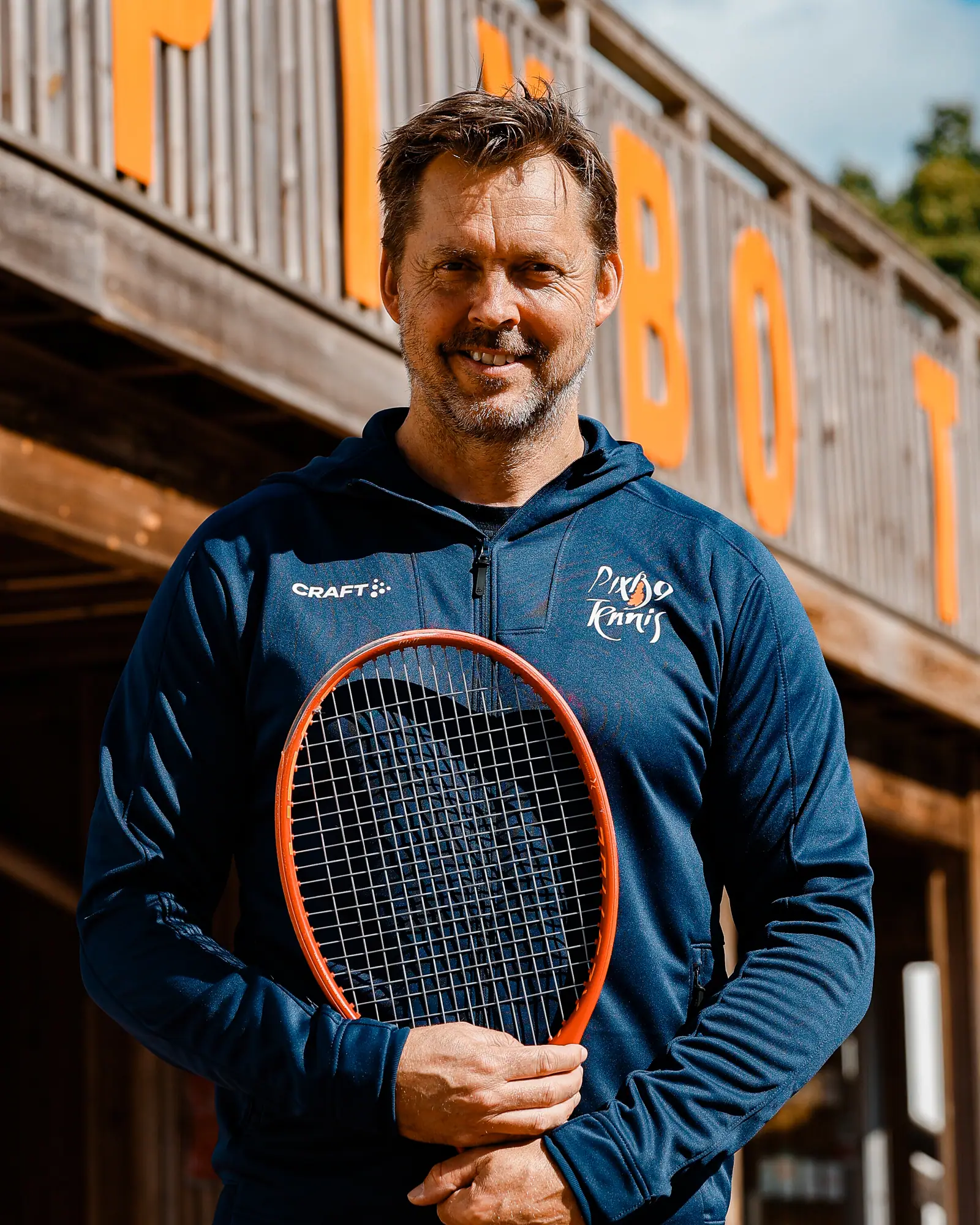 Johan Brunström, klubbchef och chefstränare, med racketen framför klubbhusets fasadtext