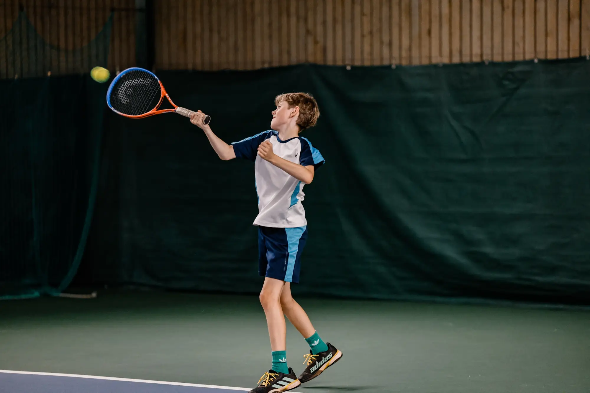 Junior slår en forehand med bollen på väg mot racketen på inomhusbanan