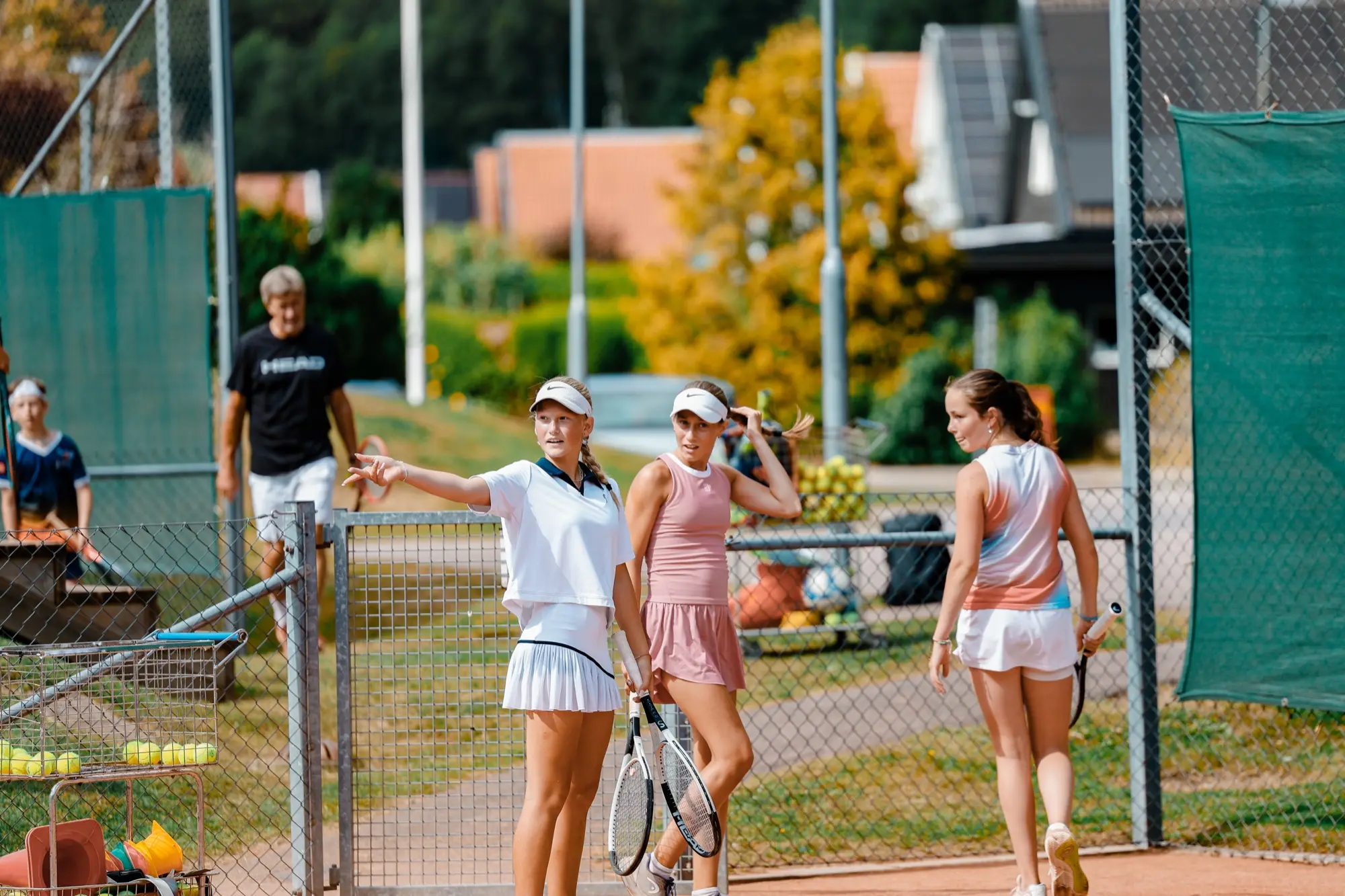 Tre juniorer med racketar står och pratar vid grusbanan efter träningen