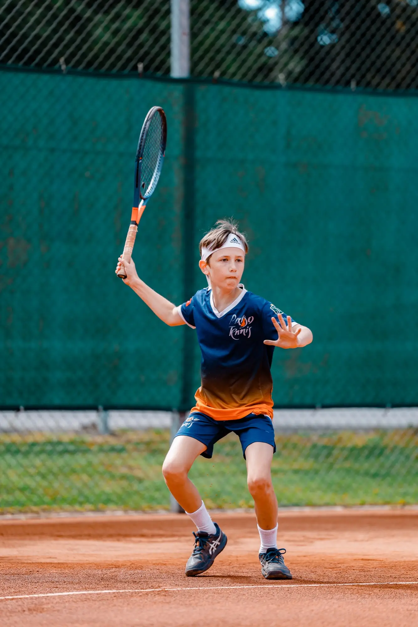Junior i klubbens tröja gör sig redo för en forehand på grusbanan