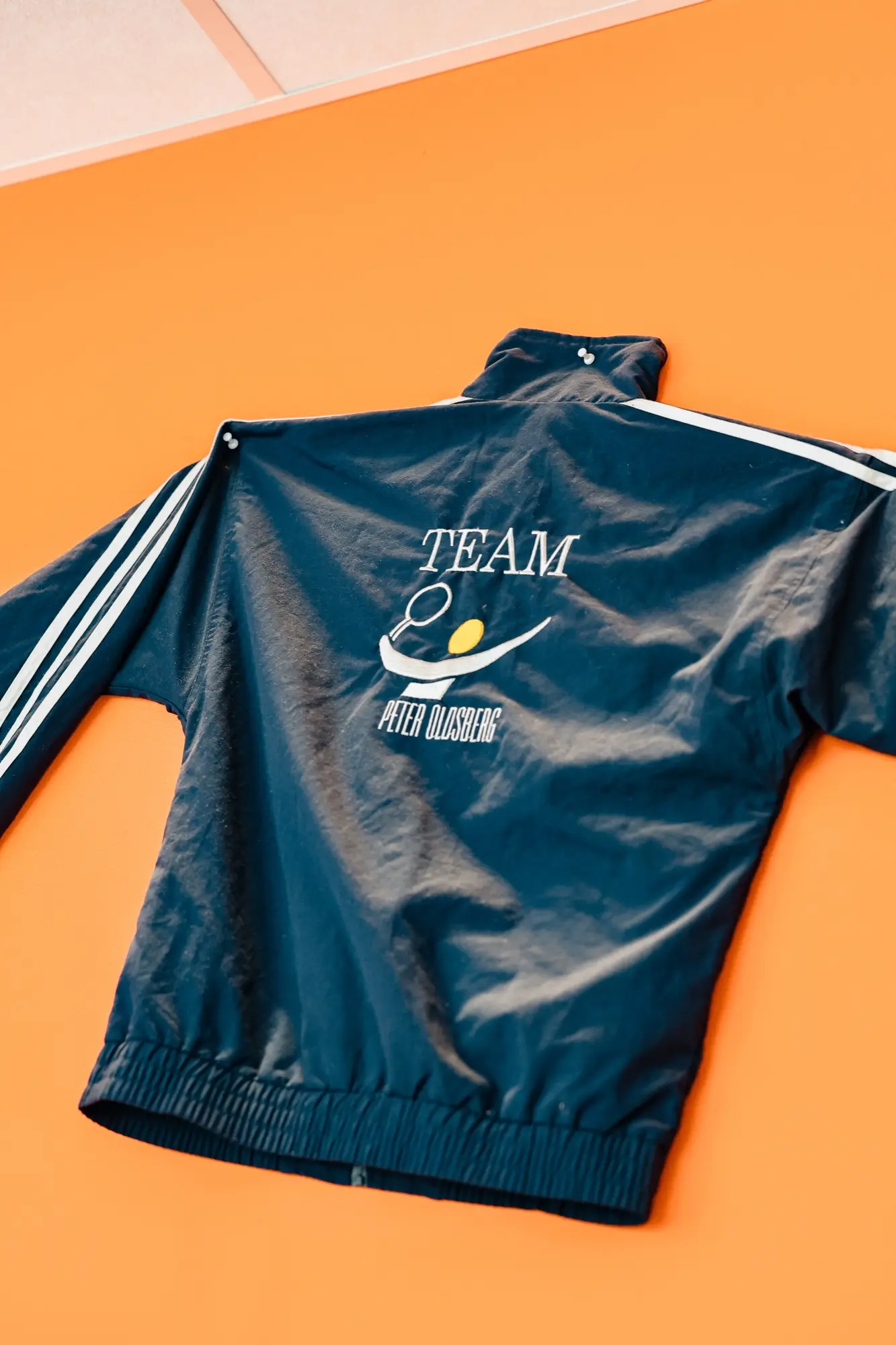 Gammal klubbjacka med texten Team Peter Oldsberg upphängd mot orange vägg