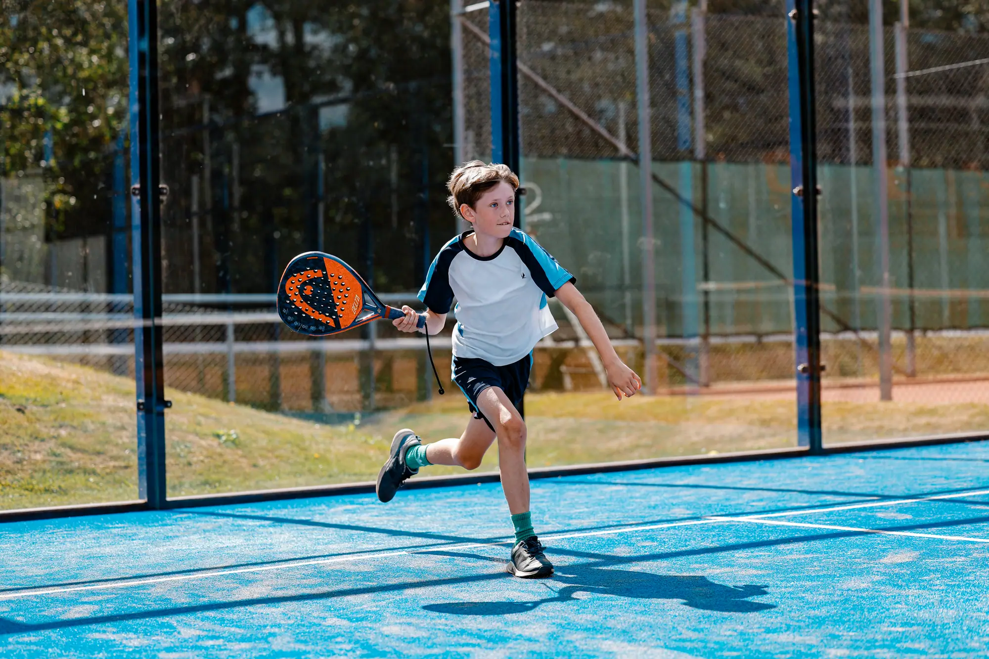 Junior i språng fram mot nätet med padelracketen i handen på den blå banan