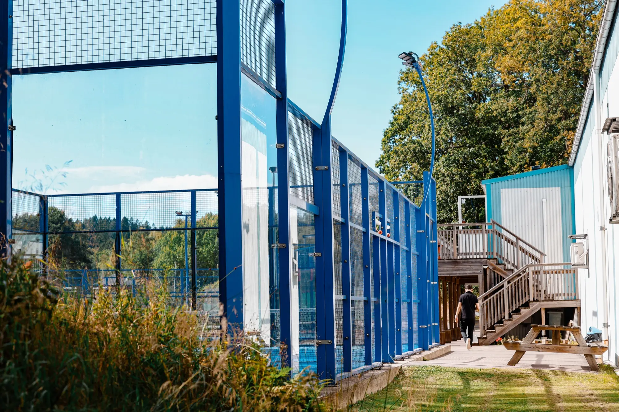 Padelbanans blå glasväggar med gången upp mot klubbhusets trappa