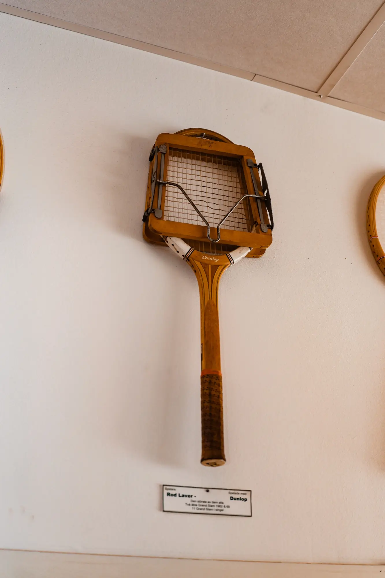Gammal Dunlop-träracket i press på väggen med en skylt om Rod Laver